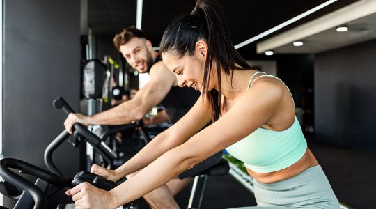 Två personer på träningscyklar i ett gym