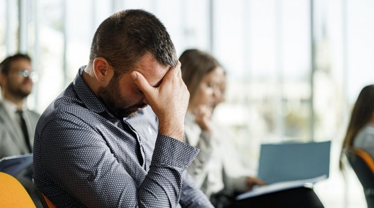 Man lutar sitt huvud i sin hand och sitter i en grupp med andra