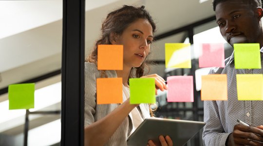 Kvinna och man diskuterar framför en glasvägg med post-it-lappar