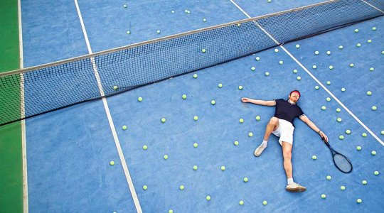 Liggande man som tappat många bollar på tennisplanen