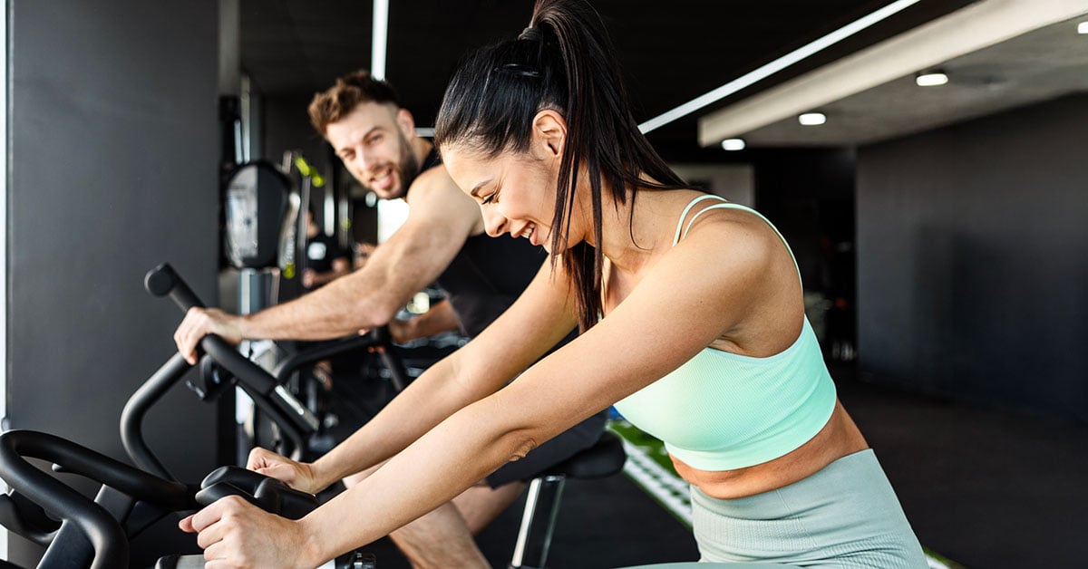 Två personer på träningscyklar i ett gym